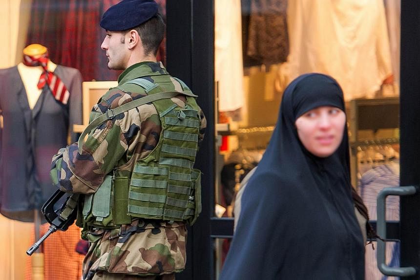 A veiled woman walks past a soldier patroling in a street of Roubaix, northern France, on Jan 13, 2015, as France announced an unprecedented deployment of thousands of troops and police to bolster security at "sensitive" sites. -- PHOTO: AFP