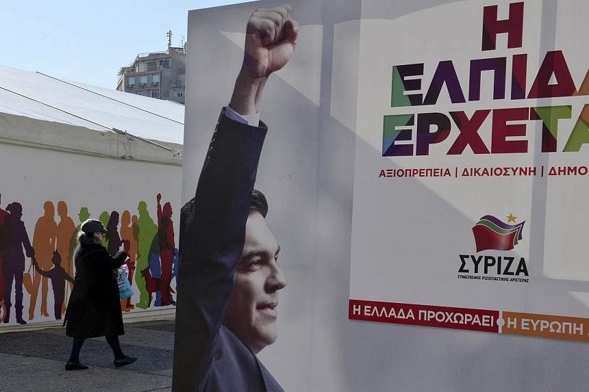 A worker hangs up an pre-election poster in front of the campaign kiosk of the anti-austerity Syriza party bearing a slogan which translates as 'the hope is coming' in central Athens on Jan 14, 2015. -- PHOTO: AFP