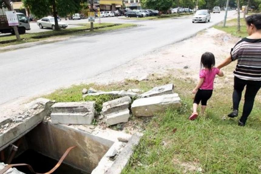 Too close to danger: Three-year-old Dhia Zhulaiqa walking with her mother near an uncovered manhole in Jalan Putra Perdana, Puchong. -- PHOTO: KAMARUL ARIFFIN / THE STAR
