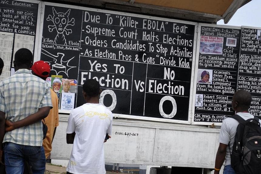 Bystanders read the headlines illustrating the battle over the holding of elections in Liberia amid the Ebola crisis at a street side chalkboard newspaper in Monrovia, Dec 2, 2014. -- PHOTO: REUTERS