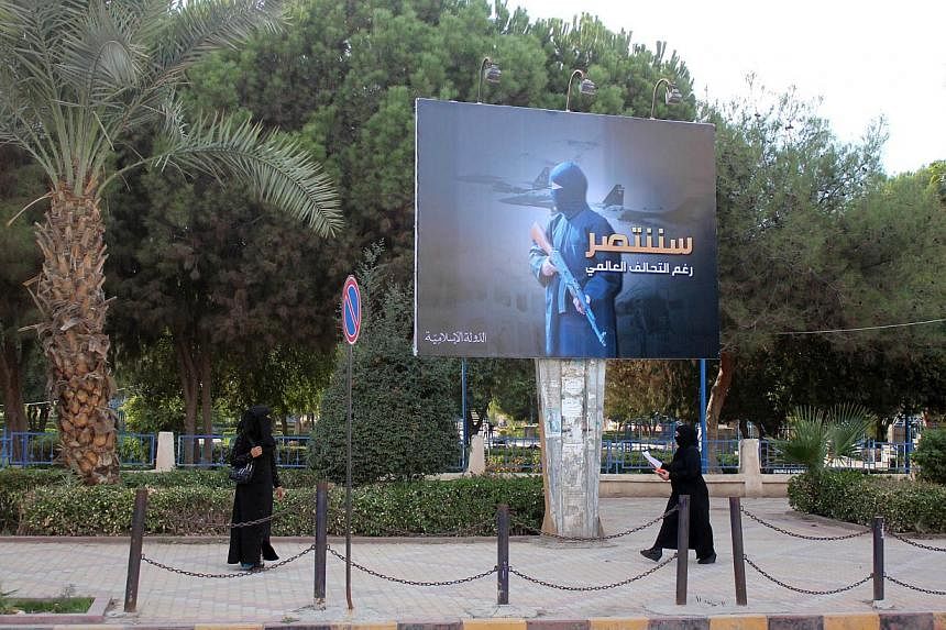 Women wearing a niqab, a type of full veil, walk under a billboard erected by ISIS as part of a campaign in the ISIS controlled Syrian city of Raqqa on Oct 1, 2014. -- PHOTO: AFP&nbsp;