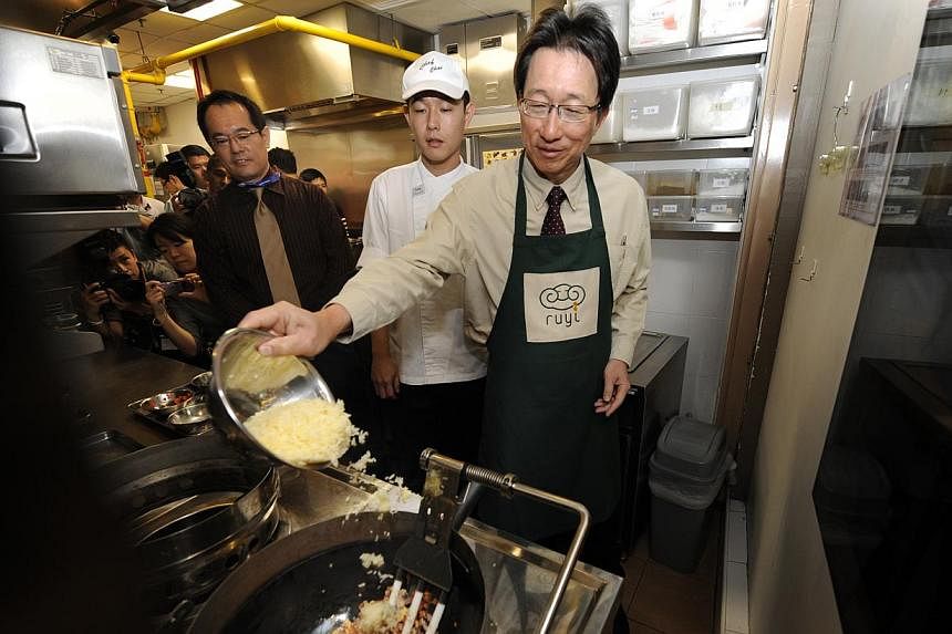 Cabinet Minister and Secretary-General of the National Trades Union Congress&nbsp;Lim Swee Say (right) adding ingredients to a robot wok that is "cooking" fried rice during a visit to Chinese fast-food chain Ruyi on Dec 6, 2010. -- PHOTO: ST FILE