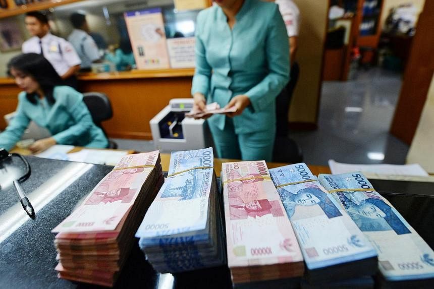 Bundles of Indonesian 100,000 rupiah banknotes and 50,000 rupiah banknotes sit on a counter at a currency exchange office in Jakarta, Indonesia. Indonesia's central bank estimates month-on-month inflation in January tumbled to near zero. -- PHOTO: BL