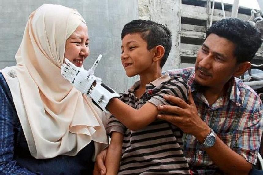 Muhammad Muqri touching his mother Nor Julaina Md Sani, 40, on the cheek with his new mechanical fingers. With them is his father Rhemi. -- PHOTO: THE STAR/ASIA NEWS NETWORK