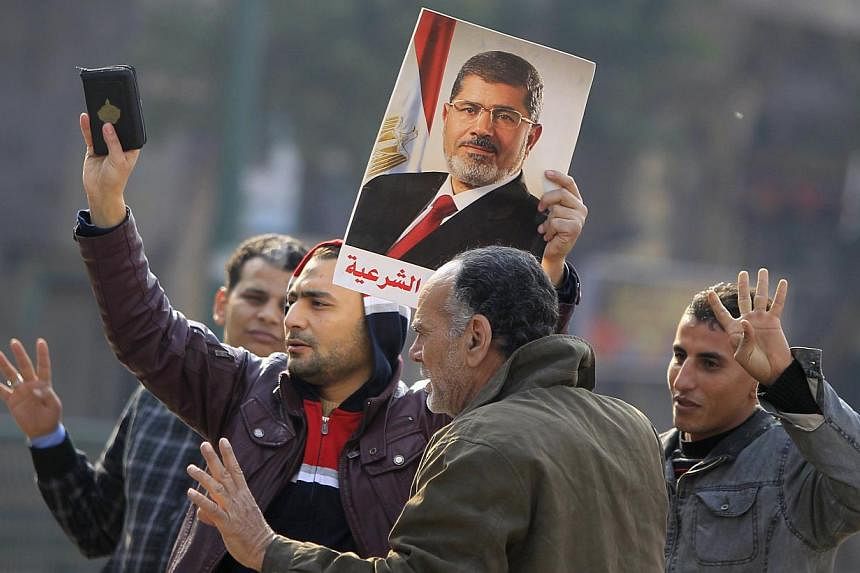 Supporters of the Muslim Brotherhood and ousted Egyptian President Mohamed Morsi hold a copy of the Koran and Morsi's picture at Talaat Harb Square, in Cairo on&nbsp;Jan 25, 2015. An Egyptian court on Monday, Feb 2, confirmed death sentences against 