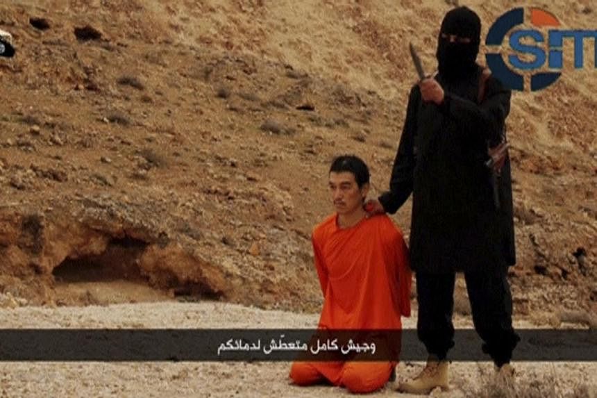 An Islamic State fighter stands next to a man kneeling on the ground purported to be Japanese journalist Kenji Goto in an unknown location in this still image from a video released by Islamic State on Jan 31, 2015. -- PHOTO: REUTERS