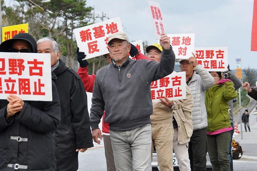 Anti-base activists hold signs reading "Stop landfill at Henoko" and "No new base", in front of a gate of the US Marine Corps' Camp Schwab at the tiny hamlet of Henoko in Nago on the southern Japanese island of Okinawa on Jan 15 in this photo taken b