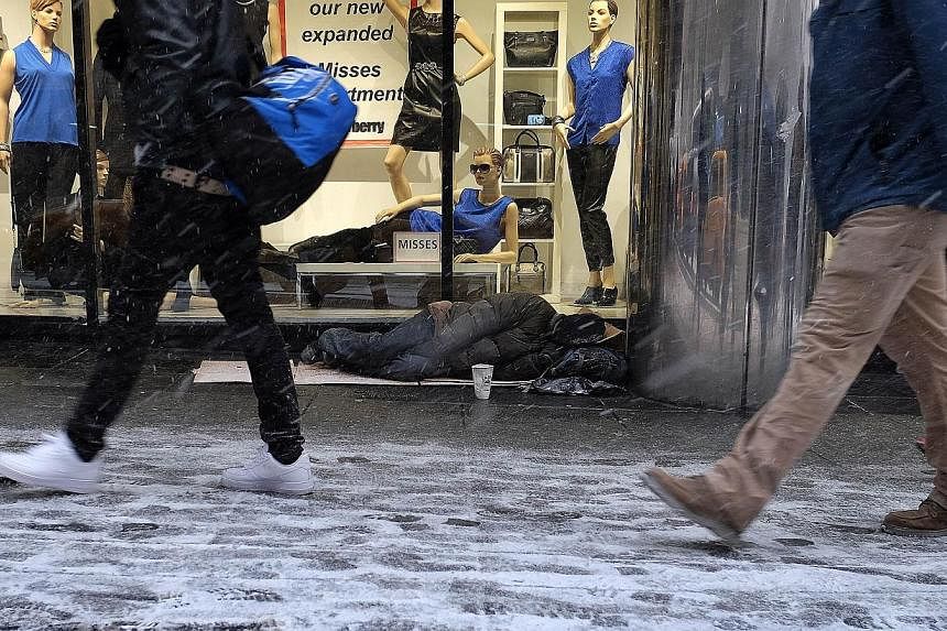 A homeless person sleeps on the sidewalk during a snow storm in New York on Jan 26, 2015. -- PHOTO: AFP