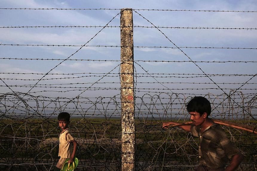 A Rohingya boy and a man walk along the fence separating Myanmar and Bangladesh on Nov 11, 2014.&nbsp;Myanmar on Wednesday, Feb 4, 2015, condemned a United Nations official for using the term "Rohingya" to describe a persecuted minority that the gove
