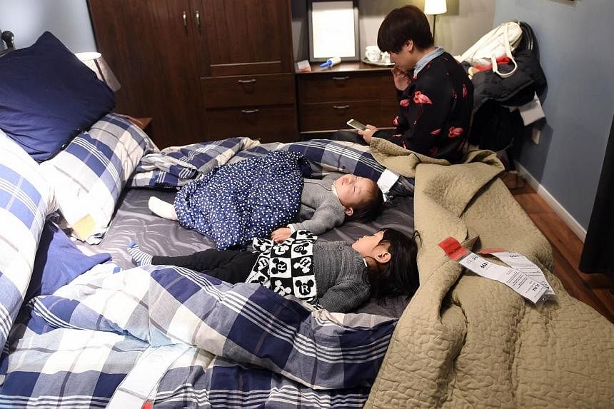 This picture taken on Jan 19, 2015, shows a Chinese woman sitting beside two sleeping babies on a display bed at a furniture store in Beijing.&nbsp;The National Sleep Foundation, an authority on official sleep guidelines in the United States, has rel