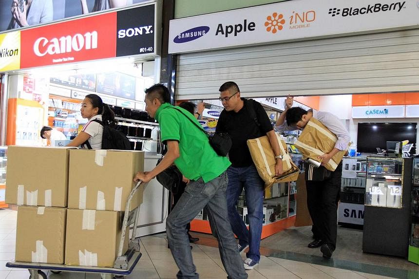 (Above) Business remains slow on the first and second floors of Sim Lim Square. (Below) Police on Nov 16 removing documents and products from Mobile Air shop, whose shady sales tactics drew complaints.