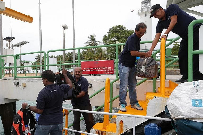 (Top) Mr V. Uthrapathi (left) taking over duties from Mr Syed Hassan, 66, at Raffles Lighthouse. (Above) Belongings being loaded and unloaded from a boat at the jetty as Mr Uthrapathi (from left) and his assistant N. Manikaveloo, 51, prepare to spend