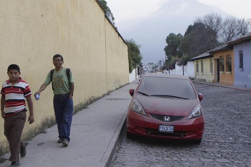 People walk near a car covered with ash in town of Antigua, on the outskirts of Guatemala City, after the Fuego volcano belched black ash into the sky on Saturday, causing the government to evacuate 100 nearby residents and forcing the closure of the