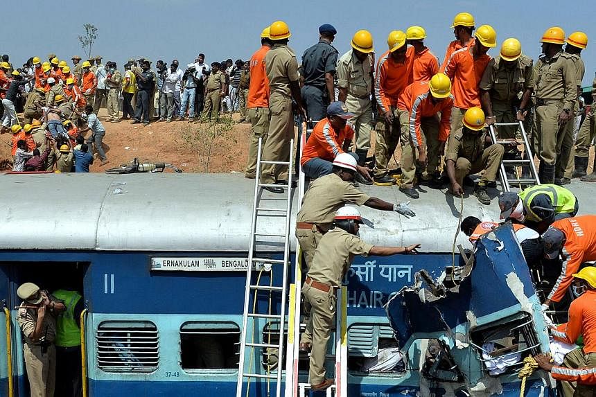 Crowds watch as Indian fire force personnel attempt to retrieve the bodies of victims from the Bangalore-Ernakulam train which derailed after a boulder fell on the track in Bidaragere, about 50 kms from Bangalore on Feb 13, 201. At least five passeng
