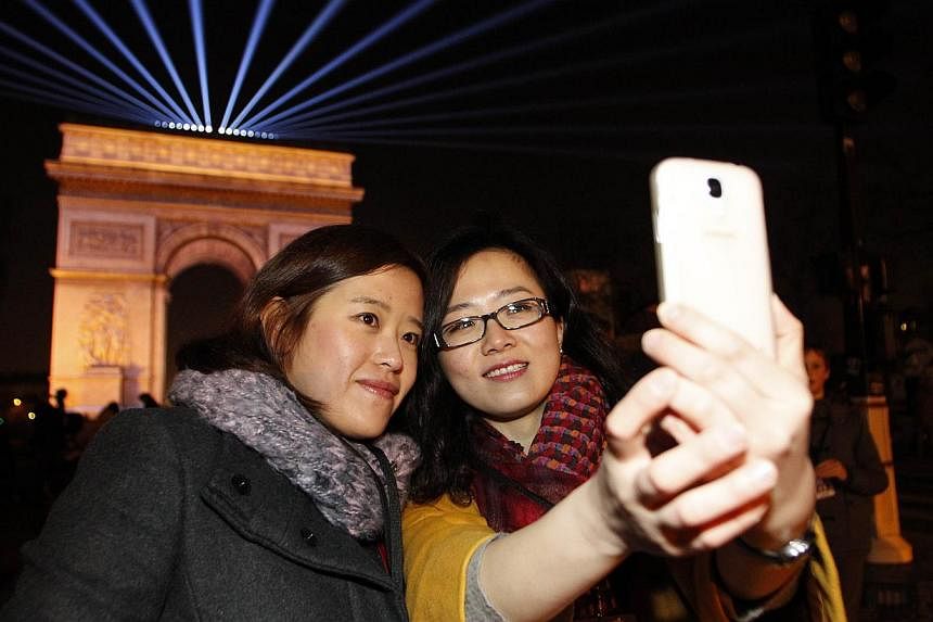Tourists tom China taking a selfie in front of the Arc de Triomphe on Champs-Elysees avenue in Paris just before midnight on Dec 31, 2014. -- PHOTO: AFP
