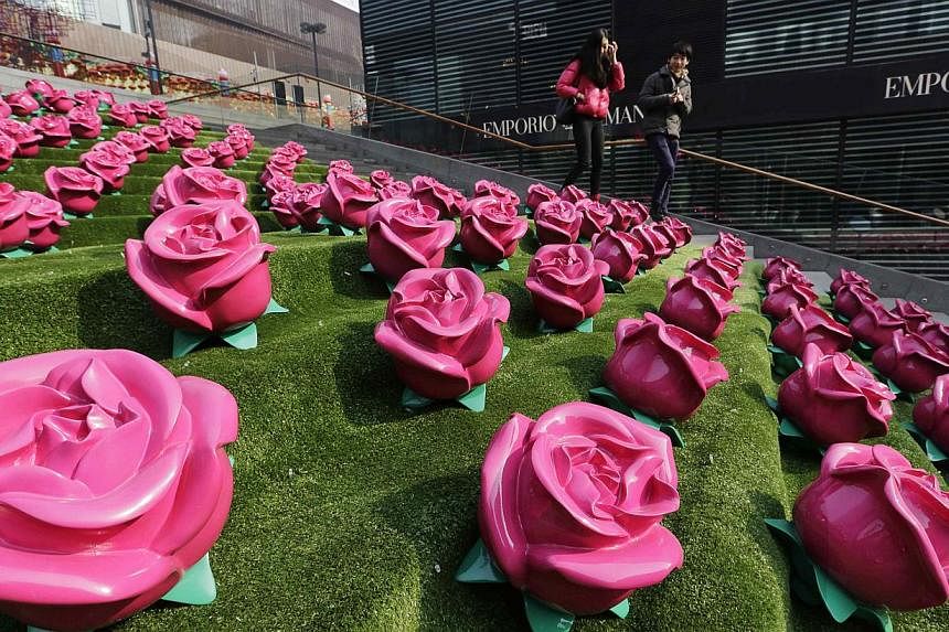 A couple walk past an installation art work of roses at a shopping centre on Valentine's Day, in Beijing on Feb 14, 2015. -- PHOTO: REUTERS