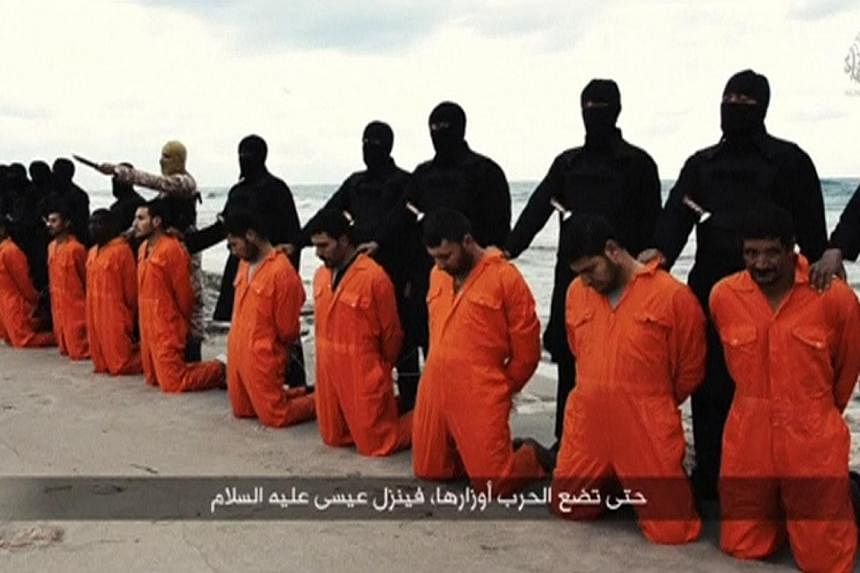 Men in orange jumpsuits purported to be Egyptian Christians held captive by ISIS kneeling in front of armed men along a beach said to be near Tripoli, in this still image from an undated video made available on social media on Feb 15, 2015.&nbsp;-- P