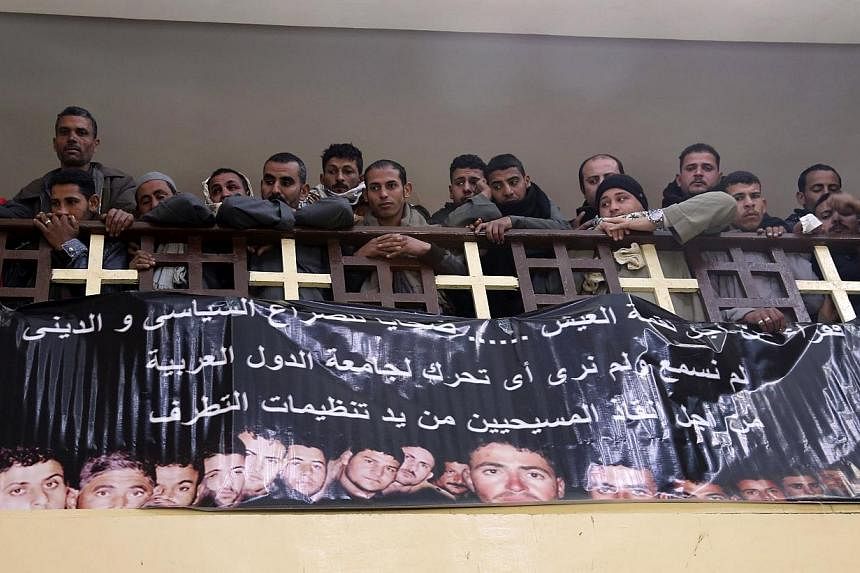 Neighbours and friends of the relatives of Egyptian Coptic men killed in Libya attend mass at a church, as a banner with pictures of the men who were men is displayed on the church wall, in El-Our village, in Minya governorate, south of Cairo Monday.
