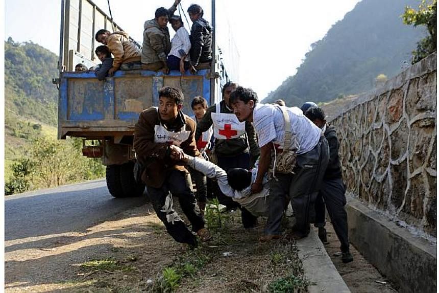 Volunteers of Myanmar Red Cross organisation carry wounded volunteer Moe Kyaw, 45, as the war victims fleeing from Laukkai sit on the truck after vehicles of rescue convoy were attacked by Kokang rebels near self-administered Kokang capital Laukkai, 