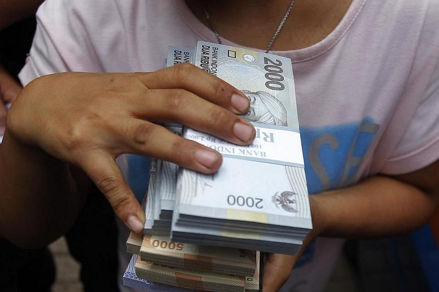 A woman holds Indonesian rupiah notes in Jakarta, on Dec 16, 2014.&nbsp;&nbsp;Indonesia's central bank unexpectedly cut its key interest rate by 25 basis points on Tuesday to spur growth as inflation slowed in Southeast Asia's biggest economy. -- PHO
