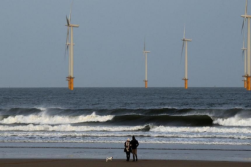 A couple walk their dog on Redcar beach past an offshore wind farm in Redcar, northeast England last month. -- PHOTO: REUTERS