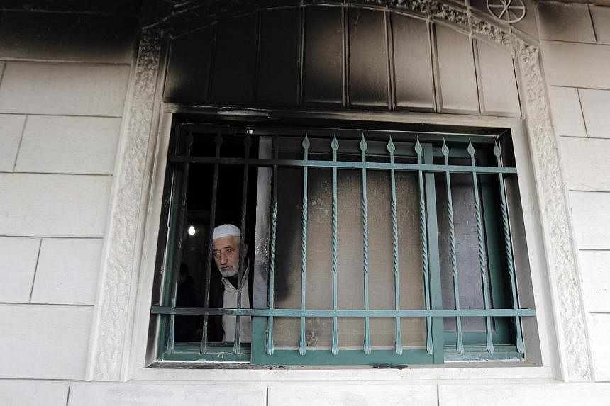 Palestinian Imam Ibrahim Abu Luha looks out a mosque window that was set alight in an overnight attack in Al-Jaba'ah village near the West Bank city of Bethlehem on Feb 25, 2015. -- PHOTO: REUTERS