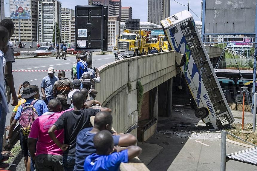 Onlookers gather on Queen Elizabeth bridge to look at a public transport bus that drove over the side of the bridge in Johannesburg, South Africa, on Feb 25, 2015. No fatal injuries were reported and the bus driver sustained minor injuries. -- PHOTO: