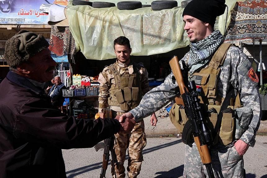 Brett (right) - a 28-year-old US national fighting ISIS militants alongside Dwekh Nawsha, a Christian militia - shakes the hand of a passer-by on Feb 5, 2015, in the northern Iraq town of Al-Qosh.&nbsp;An Australian who travelled to Syria to join Kur