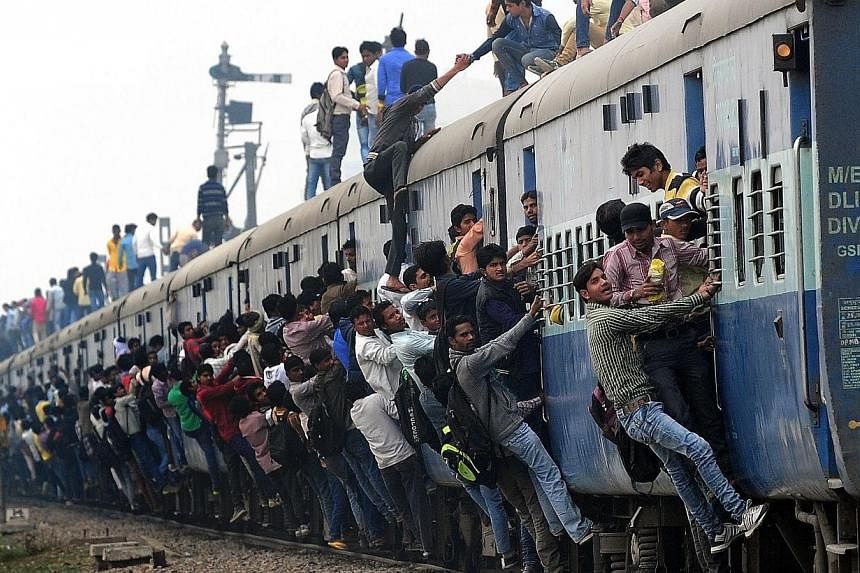 Passengers hanging onto a train as it departs from a station on the outskirts of New Delhi on Feb 25, 2015. -- PHOTO: AFP