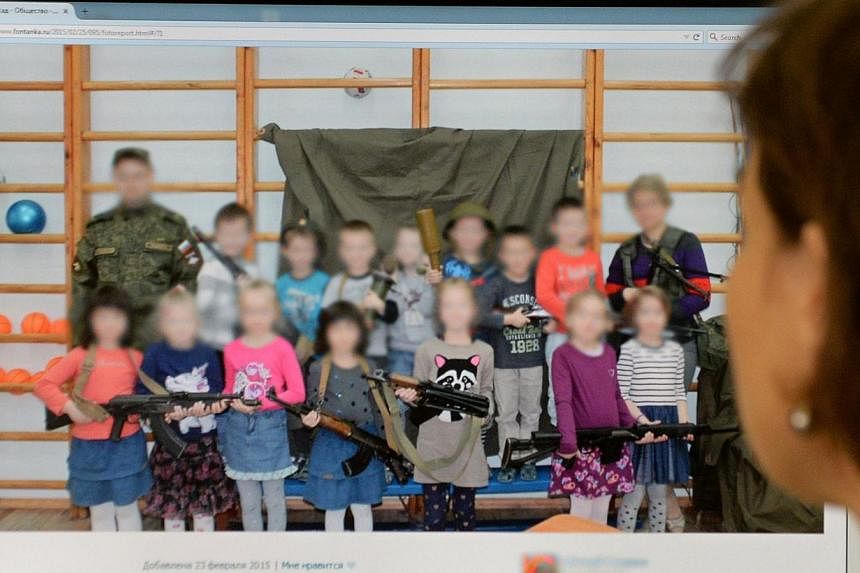 A woman looks at a computer screen displaying a photo that shows boys and girls posing with weapons at a kindergarten in Saint Petersburg, Moscow on Feb 26, 2015. -- PHOTO: AFP