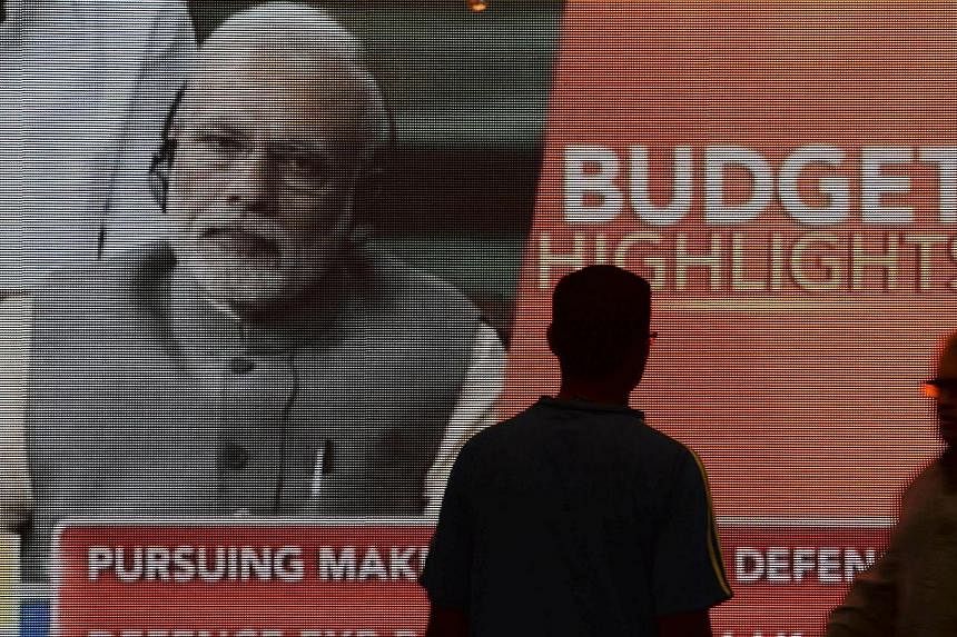 Indian office workers walk past a digital screen showing Prime Minister Narendra Modi listening to Finance Minister Arun Jaitley deliver his Budget speech at Parliament, in Mumbai on Feb 28, 2015.&nbsp;India's reform-minded prime minister appears to 