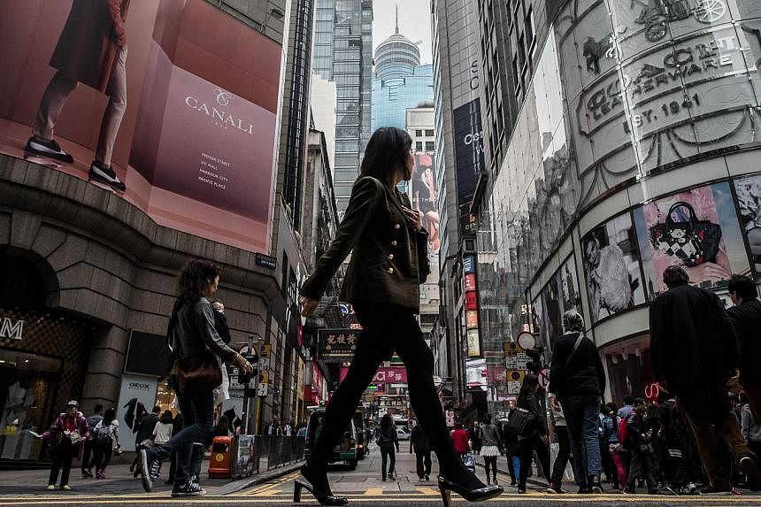 A woman crosses a street in the financial district of Central in Hong Kong on Feb 25, 2015. The Hong Kong and Singapore budgets released last week highlight some of the long-term economic challenges facing both cities - and how their respective gover