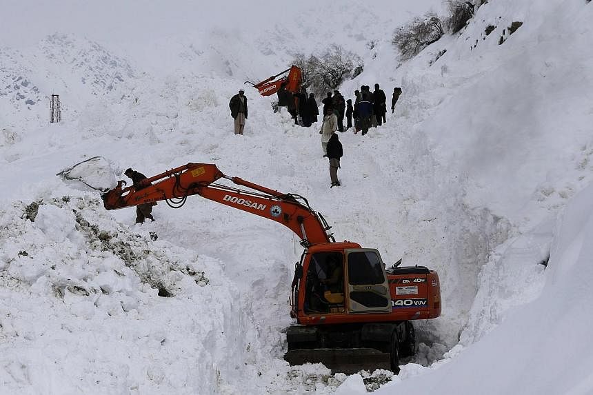 Afghan survivors of an avalanche gather as excavators clear snow from a road near Abdullah Khil village in the Dara district of Panjshir province on March 1, 2015. -- PHOTO: REUTERS