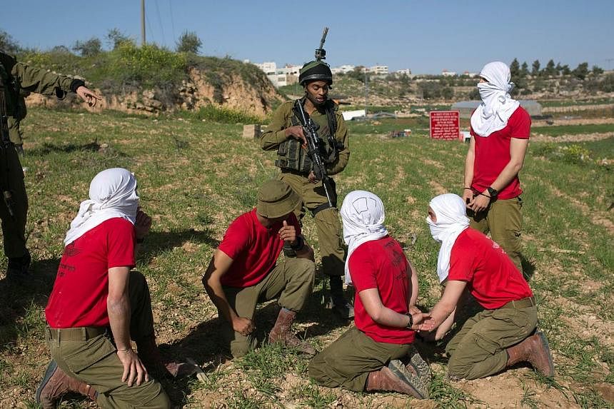 Israeli soldiers detain soldiers in red T-shirts, playing the role of Palestinian rioters, during a drill near the West Bank city of Hebron on Sunday, organised by the Israeli army to simulate dispersing of riots and crowd control. -- PHOTO: AFP