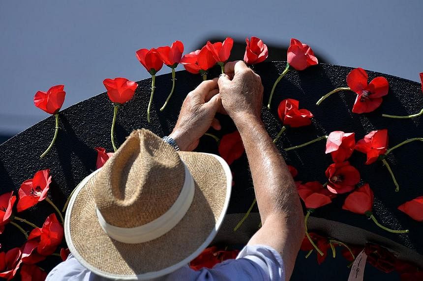 A visitor pays his respect to Australia's Anzac soldiers as he pins a poppy to the Wall of Remembrance in front of the Queen Elizabeth cruise ship in Sydney on March 3, 2015. Red poppies were placed on the Wall of Remembrance for each of the 11,500 A