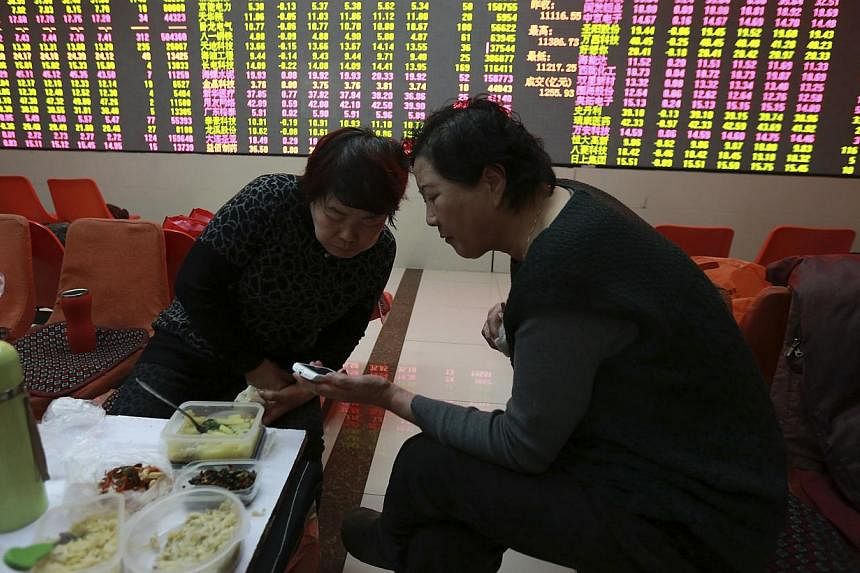 Investors look at a mobile phone as they have lunch in front of an electronic board showing stock information at a brokerage house in Shenyang, Liaoning province on&nbsp;Feb 5, 2015. China's stocks fell, erasing the benchmark index's gain for the yea