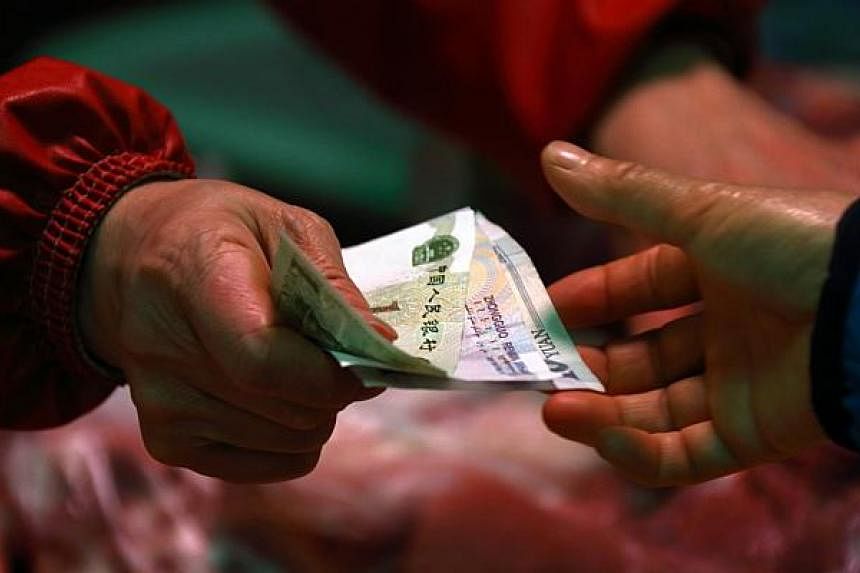 A woman holds Chinese yuan banknotes as she buys pork at a market stall in Beijing, China, on March 4, 2015.