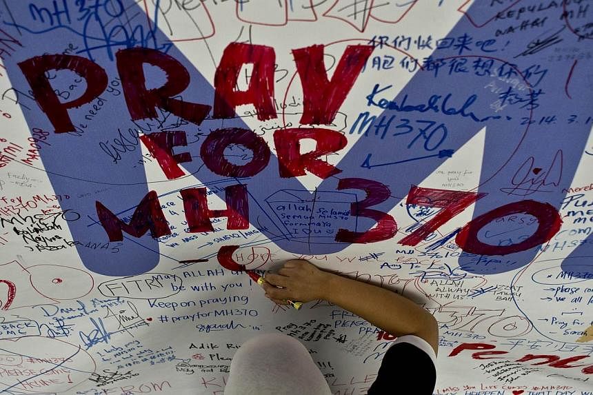 A file photo taken on March 14, 2014 shows a Malaysia Airlines employee writing a message expressing prayers and good wishes for passengers onboard missing Malaysia Airlines Flight MH370 at Kuala Lumpur International Airport in Sepang. -- PHOTO: AFP