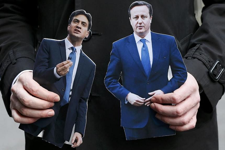 A journalist standing in Downing Street holding cardboard cutouts of Britain's Prime Minister David Cameron (right) and Ed Miliband, the leader of the opposition Labour Party, in central London on March 18, 2015. Mr Cameron will face off against six 