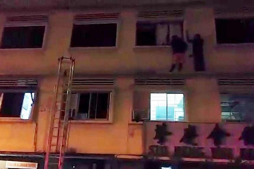 Two foreign workers who went out on the ledge on the third floor of the apartment in 35 Geylang Lorong 4 on December 7,2014, trying to get to safety from the fire that broke out on the ground floor. Four foreign workers died in the fire. -- PHOTO: SH