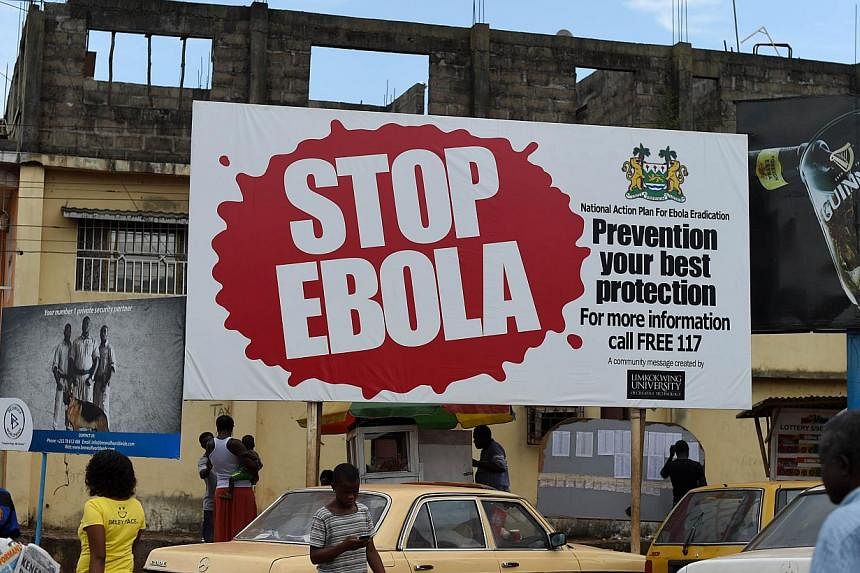 A picture taken on Nov 7, 2014, shows people walking past a billboard with a message about ebola in Freetown, Sierra Leone. -- PHOTO: AFP