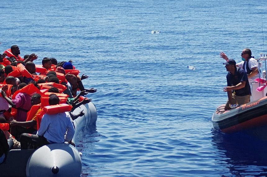 A handout picture made available on May 2, 2015 of Migrant Offshore Aid Station (MOAS) employees throwing bottles of water from a dinghy of the ship 'Phoenix' to refugees in a rubber raft off Malta, on August 30, 2014. -- PHOTO: EPA&nbsp;