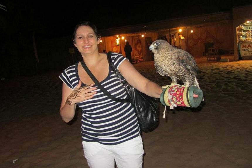 Ms Katherine Cole extending a hand to a bird of prey at a falcon show in the Arabian Desert.
