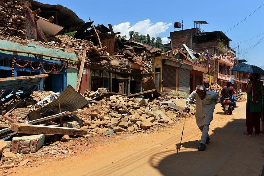 People walking past damaged houses at Trishuli in Nuwakot district north of Kathmandu on May 4, 2015. Nepali police and local volunteers found the bodies of about 100 trekkers and villagers buried in an avalanche set off by last month's devastating e