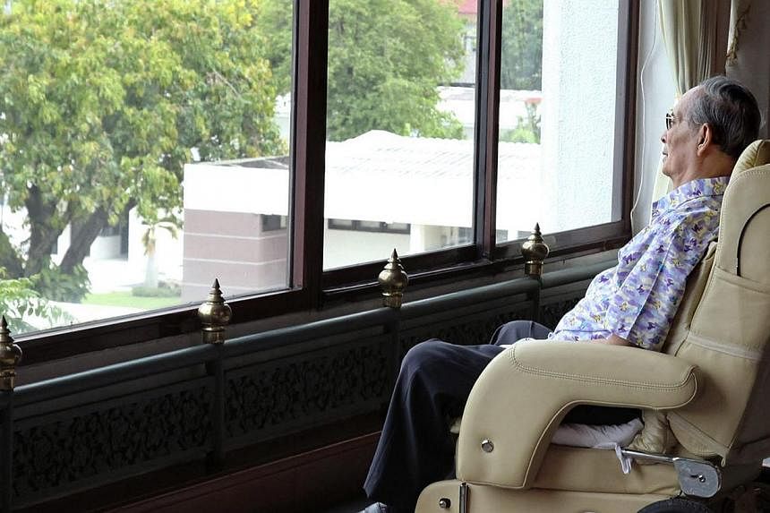 A handout photograph made available by Thailand's Royal Household Bureau on April 25, 2015, shows Thai King Bhumibol Adulyadej sitting on a wheelchair as he looks from a window at the Royal Navy Auditorium in Bangkok, Thailand, on April 23, 2015. -- 