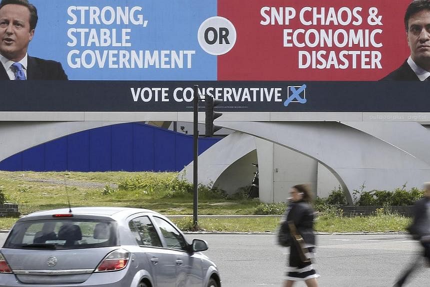 People walk under a conservative advertising hoarding, featuring David Cameron and Labour party leader, Ed Miliband, on a major road junction near to central London, Britain on May 6, 2015.&nbsp;Campaigning in Britain's most unpredictable election in