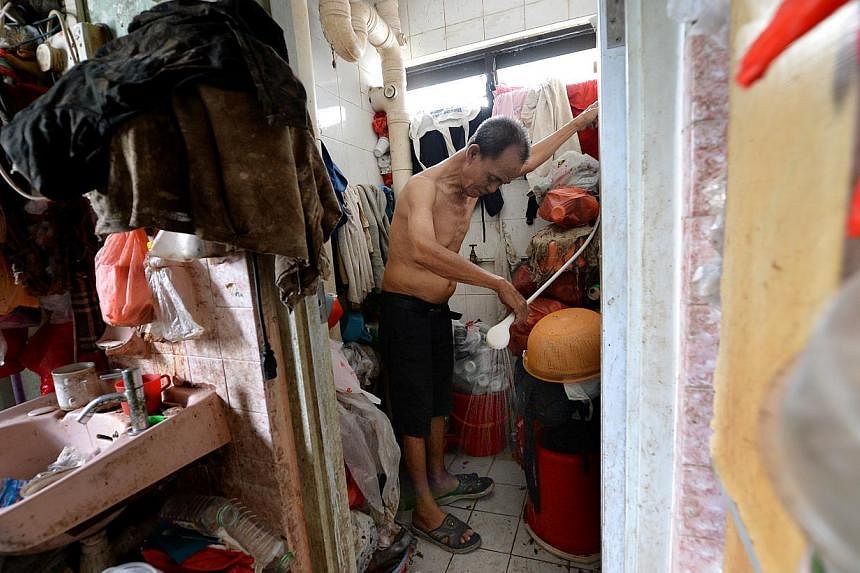 Mr Lim Chin Ting demonstrating how he showers every day in a toilet that is filled with junk. Mr Lim, a drinks assistant at a coffee shop nearby, has to live in a three-room flat that is filled with junk at Block 19 Eunos Crescent because his wife, M
