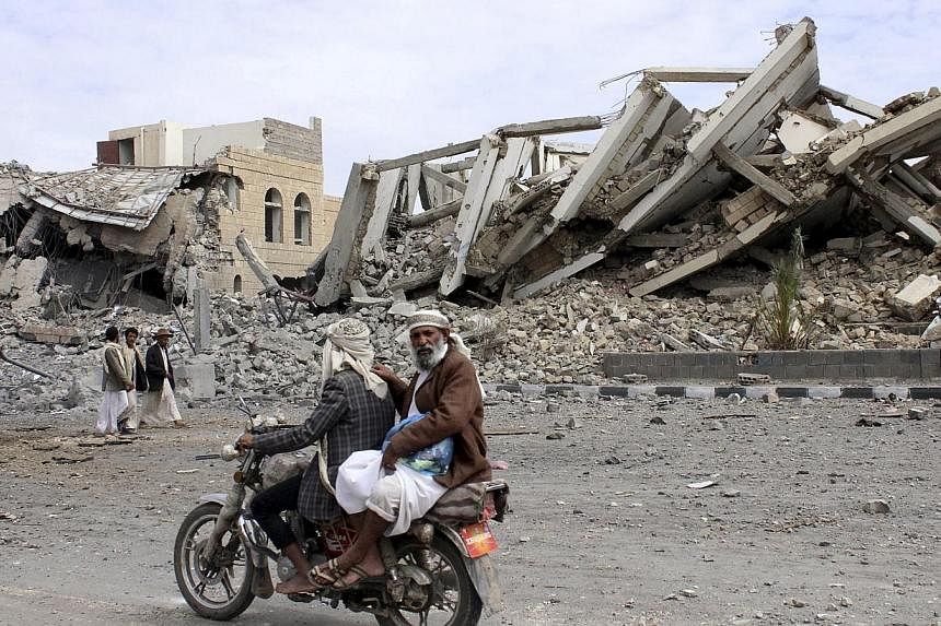People ride on a motorcycle as they pass by a police headquarters destroyed by a Saudi-led air strike in Yemen's northwestern city of Saada on May 7, 2015. -- PHOTO: REUTERS