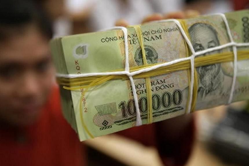 A bank teller holding up a bundle of Vietnamese dong in Ho Chi Minh City. Vietnam devalued the dong for the second time this year on Thursday to support exports and curb import demand which has left it with a trade deficit. -- PHOTO: BLOOMBERG&nbsp;