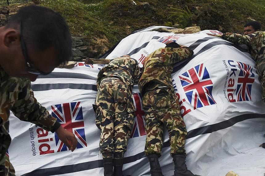 Nepali soldiers lay on a tarp covering food aid as they try to protect it from the rotor wash created by a Chinese transport helicopter during relief operations in the north-central village of Dunche in Nepal. Nepal's government said on Sunday, May 1